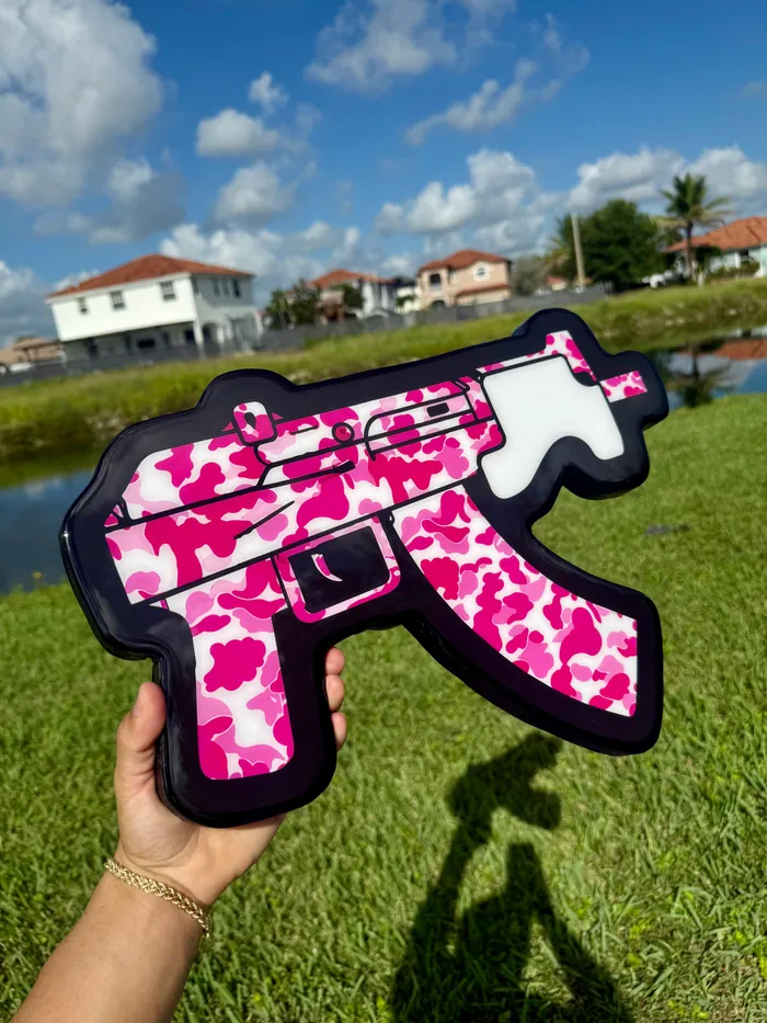 A pink camouflage rifle silhouette in glossy epoxy, held up against the sky